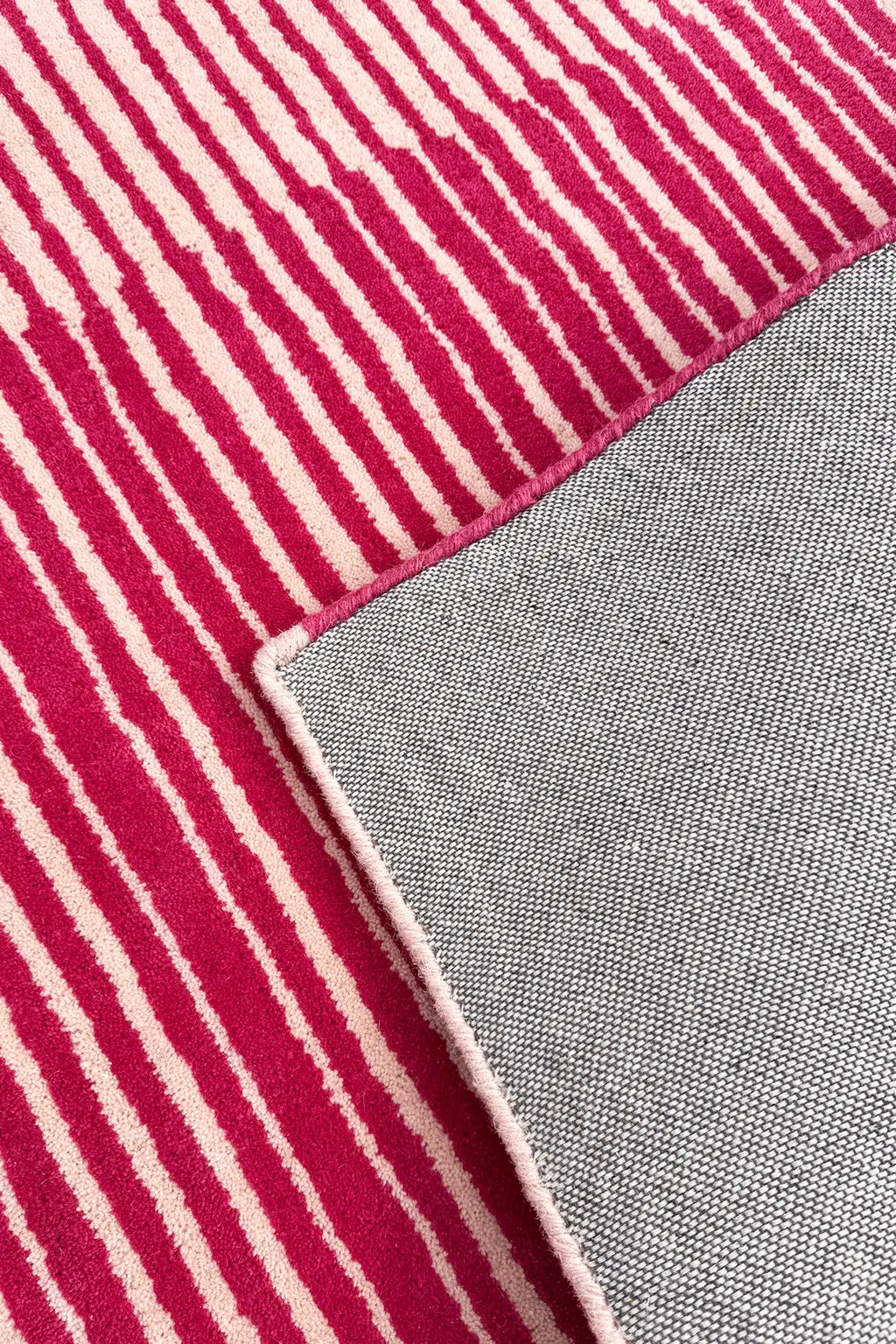 Close-up of a hot pink and white striped rug with a gray fabric surface.