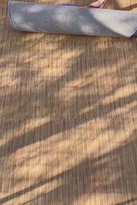 Irregular blue rug being unrolled in sunlight across wooden floor