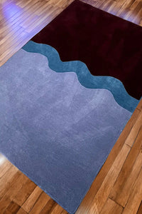 Purple and chocolate brown wavy modern area rug styled on hardwood floor, shown in cozy minimalist bedroom setup