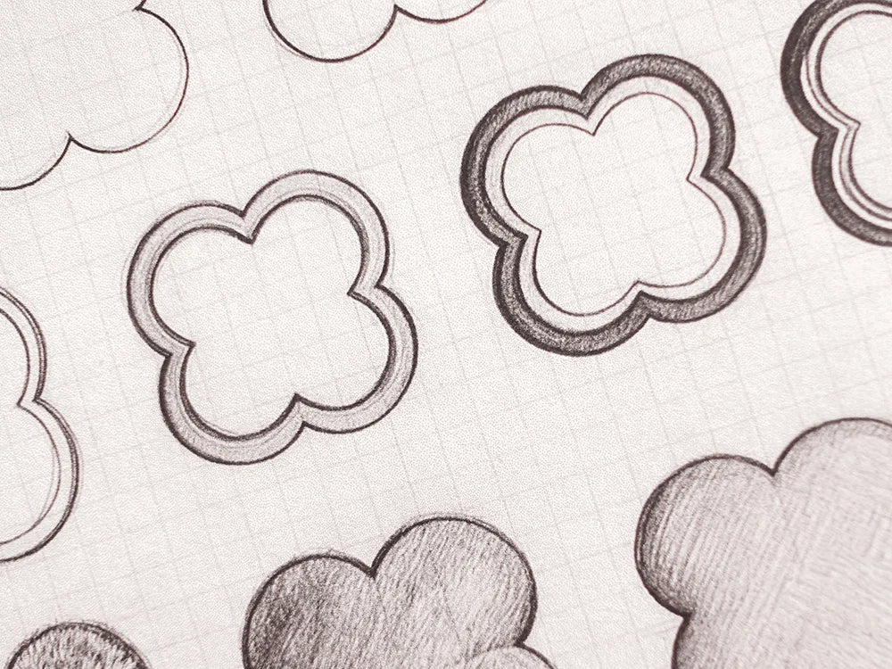 A close-up of a white paper surface with a repeating pattern of hand-drawn cloud-like shapes outlined in black and shaded in gray.