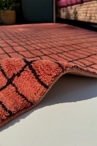 Close-up of a textured rust red rug with black lines on a light surface.