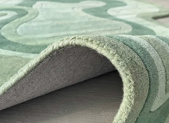 Close-up of a textured green rug with wavy patterns on a wooden floor.