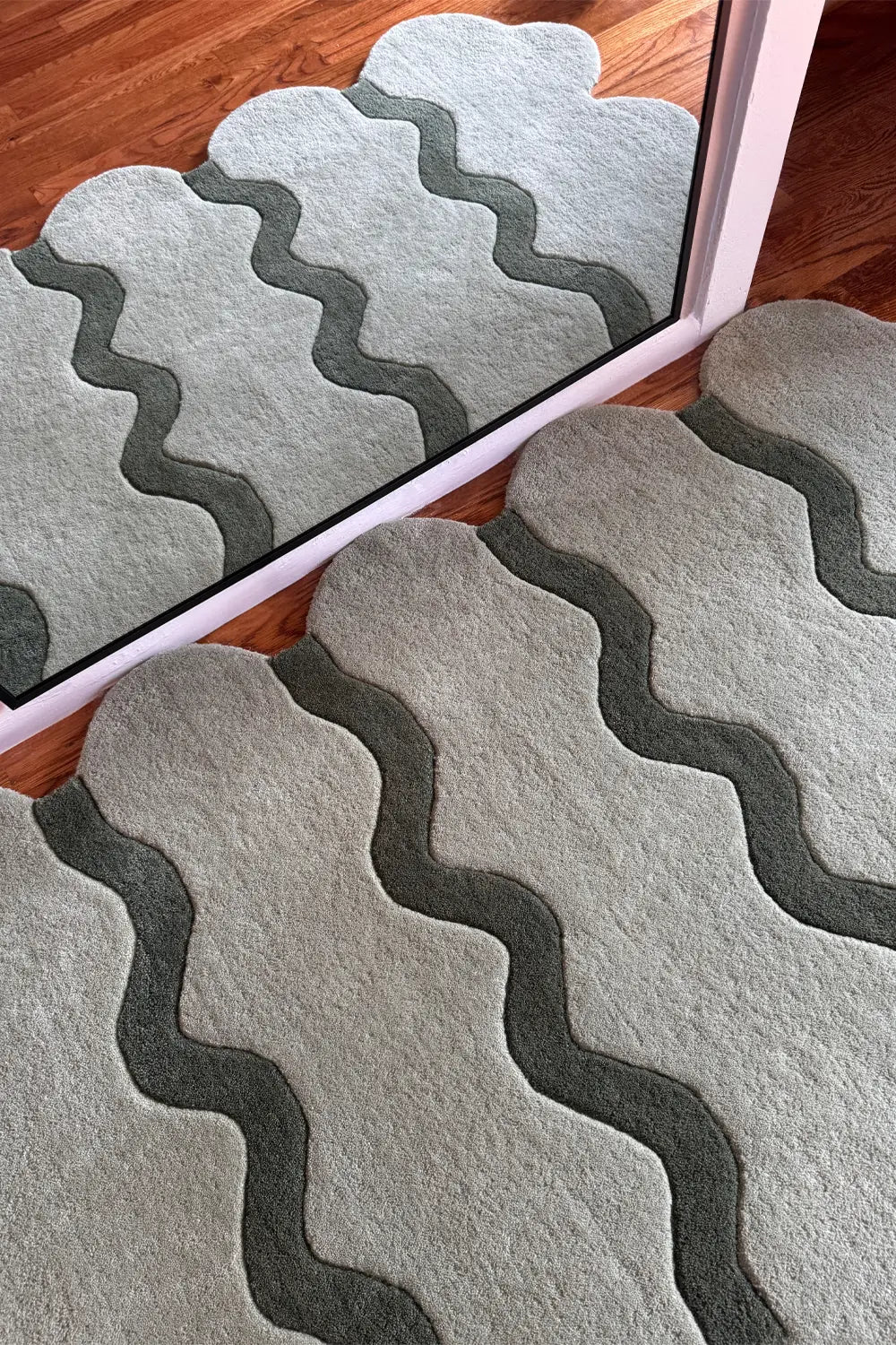 Overhead view of the Sculpted Edge Rug in sage green with scalloped edges and wavy stripes.