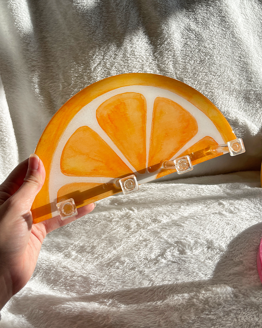 Hand-painted orange slice key holder with vibrant colors, made from wood and resin, featuring four clear hooks.