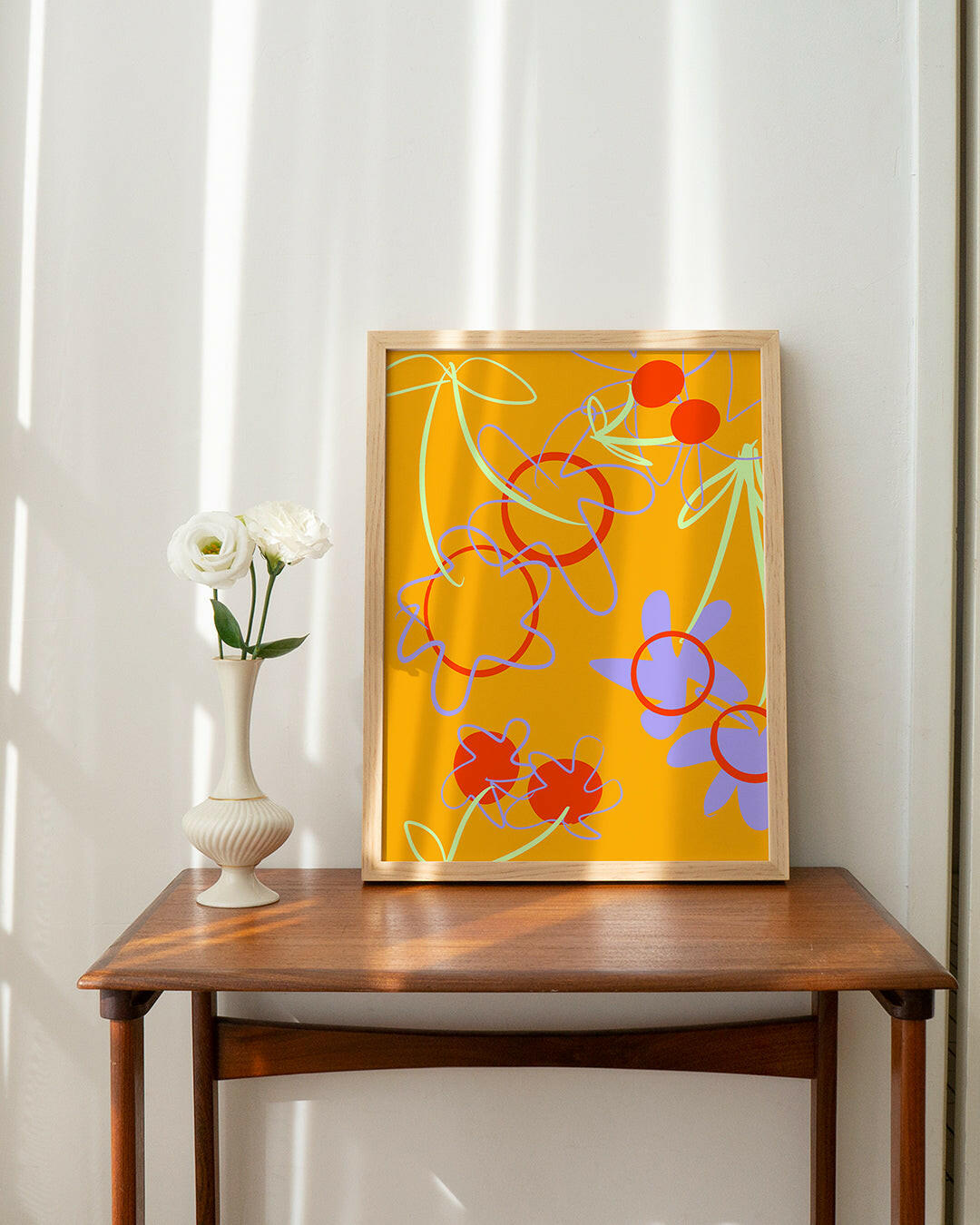 Wall art of an abstract cherry and flower design. Shown framed and resting on a desk.