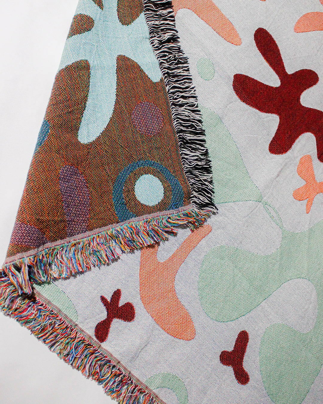 Amoeba Party Cotton Woven Throw Blanket with a blend of colors and fringe edges.